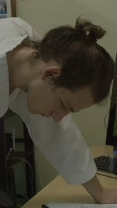 a woman in white shirt writing on paper next to laptop