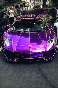 a purple lamb car parked in front of a building with people standing around it and looking at the cars