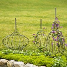 three metal vases sitting on top of a lush green grass covered field next to rocks