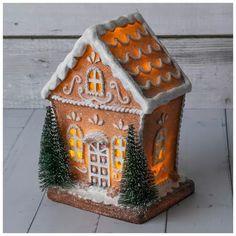 a lighted gingerbread house with trees and snow on the roof is sitting on a white wooden floor