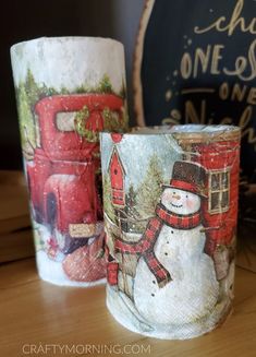 two christmas themed candles sitting on top of a wooden table