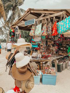 many hats and bags are on display at the beach market, with palm trees in the background