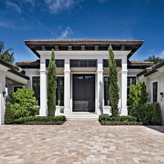 a large white house with two black doors and some bushes on the side of it