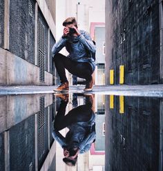 a man kneeling down in front of a puddle taking a photo with his cell phone