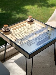 a glass table with a keyboard on it in front of a window overlooking the grass