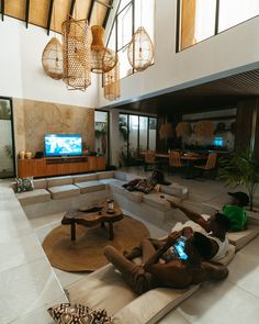 two people sitting on couches in a living room with a television and large windows