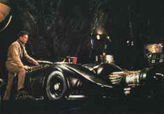 a man standing next to a batmobile in the dark knight film batman returns,