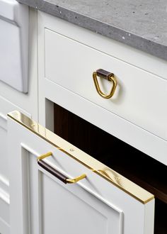 a white kitchen with marble counter tops and gold handles on the drawer pulls that are open