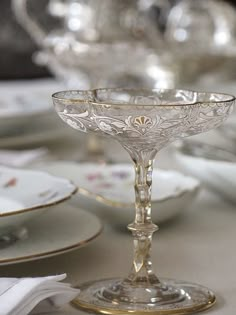 a fancy glass goblet sits on a table with other plates and silverware