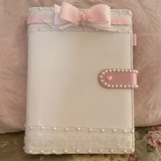 a pink and white book with a bow on the front is sitting on a bed