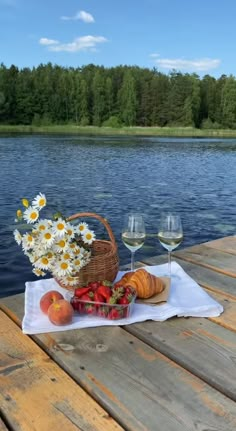 two glasses of wine and some food on a table near the water with daisies