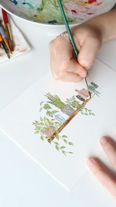 a child's hand holding a pencil and drawing on paper with watercolors