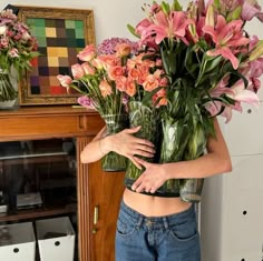 a woman is holding two vases with flowers in them and her hands behind her back