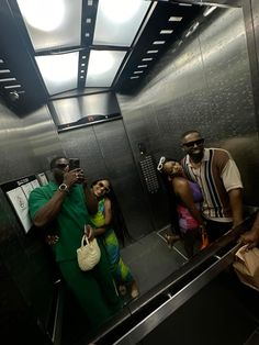 two men and a woman taking pictures in an elevator stall with their cell phones up