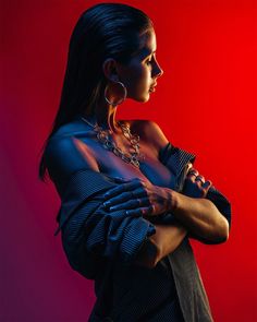 a woman with her arms crossed standing in front of a red background, wearing earrings