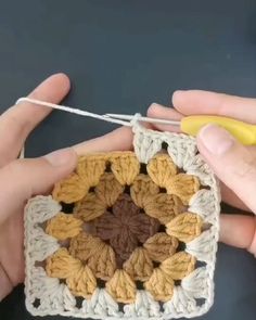 someone crocheting a square with two hands and a yellow object in the background