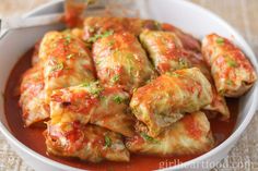 a white bowl filled with stuffed cabbage rolls covered in marinara sauce and parmesan cheese