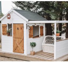 a small white shed with wooden doors and shutters on the outside, next to a deck