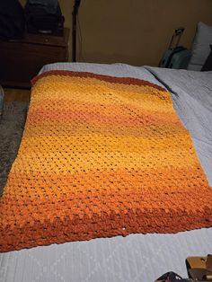 an orange and yellow crocheted blanket on top of a bed