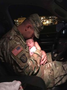 a soldier holding a baby in his lap while sitting in the back seat of a car