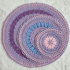 two circular crocheted doilys sitting on top of a white blanket covered in purple and blue yarn