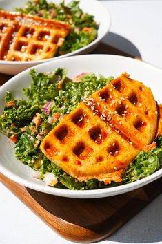 two white plates with waffles and greens on them