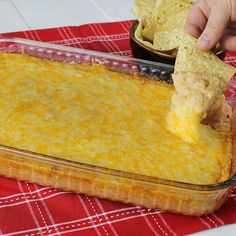 a person dipping a tortilla chip into a casserole dish with cheese