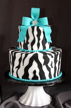 a zebra print cake with turquoise ribbon and bow on top, sitting on a pedestal