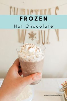 a person holding up a drink with whipped cream and chocolate on top, in front of a sign that reads frozen hot chocolate