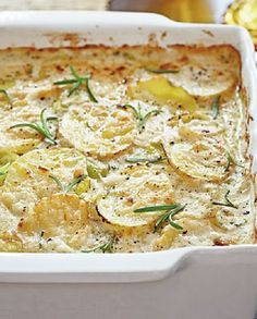 a casserole dish with potatoes and herbs in it on a table next to silverware