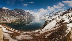 a lake surrounded by snow covered mountains under a blue sky with white clouds in the background