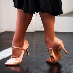 a woman's legs in high heeled shoes on a black floor with white walls behind her