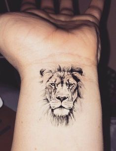 a small tattoo on the wrist of a woman with a lion head in black ink