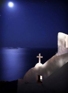 a cross on the side of a building with water in the background at night time