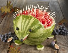 a watermelon sculpture with spikes on it's head and fruit in the background