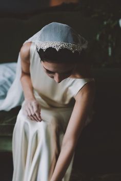 a woman in a white dress sitting on a couch wearing a tiara and holding her hands together