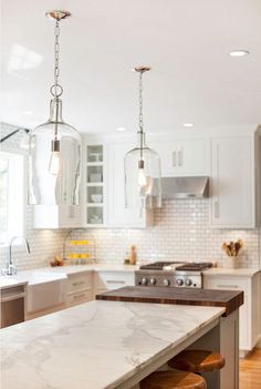 a kitchen with marble counter tops and two pendant lights hanging from it's ceiling