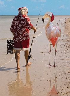 a man standing on top of a sandy beach next to a flamingo holding a fishing pole