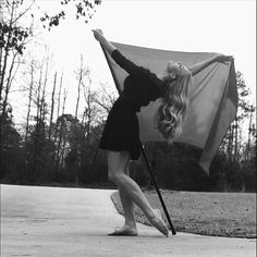 a woman is holding an umbrella on the sidewalk in front of trees and grass with her legs spread out