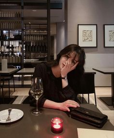 a woman sitting at a table with a glass of wine in front of her face