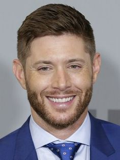 a man in a blue suit and tie smiling at the camera with his eyes closed