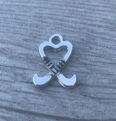 a silver charm with a heart and two crossed swords attached to it on a gray surface