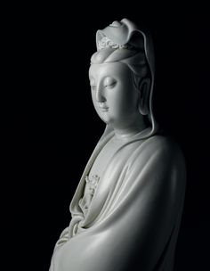 a white buddha statue sitting on top of a black surface with its eyes closed and hands clasped