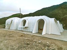 several white domes sitting on top of a dirt field next to a mountain covered in green hills