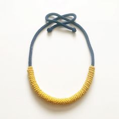 a yellow and blue necklace on a white surface with a knot at the end of it