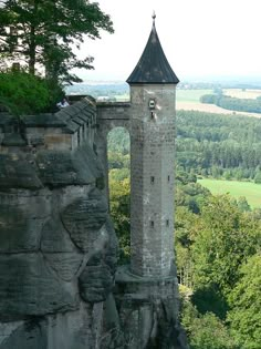 a tall tower sitting on the side of a cliff next to a lush green forest