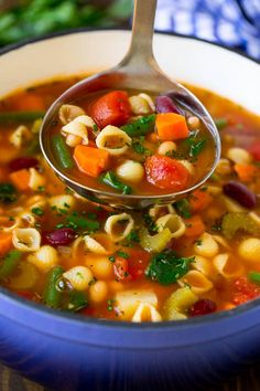 a ladle full of pasta soup with vegetables being held up by a metal spoon