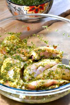 a glass bowl filled with chicken covered in pesto next to a bowl of seasoning