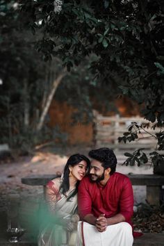 a man and woman sitting next to each other under a tree