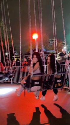 two young women sitting on swings in the middle of an amusement park at night time